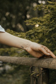 A close-up photograph of a hand with a 'Vida' tattoo resting on a wooden rail.