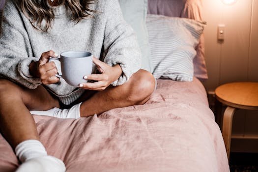 A woman enjoys a warm drink in bed, wearing a cozy sweater and socks. Intimate and relaxed atmosphere.