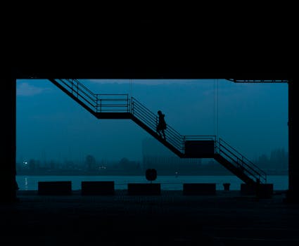 Silhouetted woman walking up stairs in an urban setting during dawn over a river.