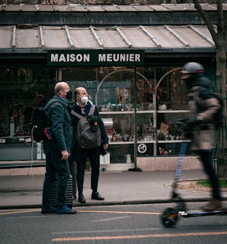 Street view of two adults standing by a shop as an electric scooter passes by.