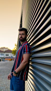 Young male model in a striped shirt posing against a modern building during sunset in Porto, Portugal.